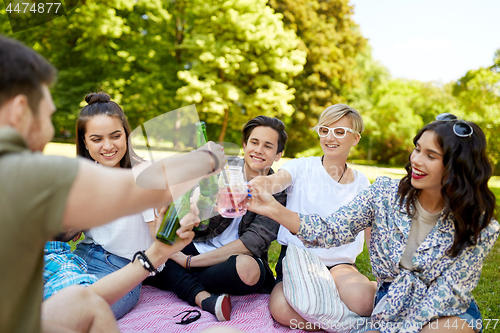 Image of happy friends clinking drinks at summer park