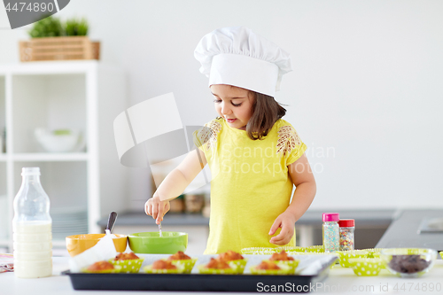 Image of little girl in chefs toque baking muffins at home