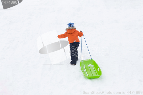 Image of little boy with sled climbing snow hill in winter