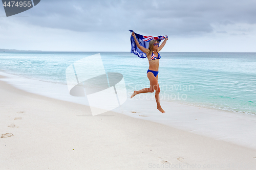 Image of Aussie girl running on white sandy beach with flag