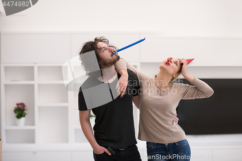 Image of couple in party hats blowing in whistle