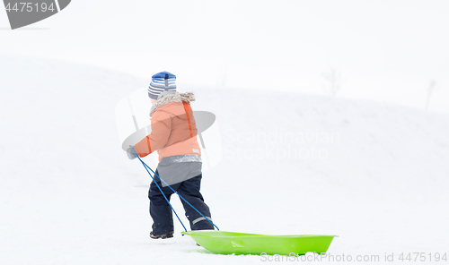 Image of little boy with sled climbing snow hill in winter