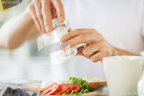 Image of close up of male hands seasoning food by salt mill