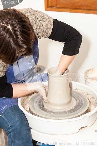 Image of Female Potter creating a earthen jar on a Potter\'s wheel