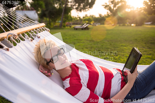Image of woman using a tablet computer while relaxing on hammock