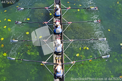 Image of Four Womens rowing team on blue lake, Aerial view