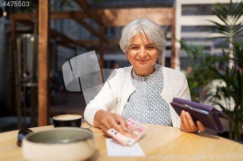 Image of senior woman with money paying bill at cafe