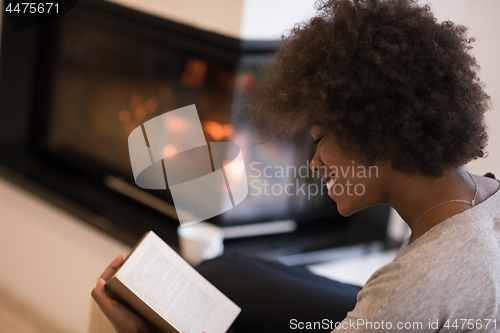 Image of black woman reading book  in front of fireplace