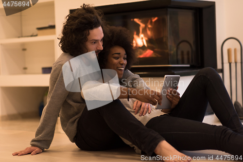 Image of multiethnic couple using tablet computer on the floor
