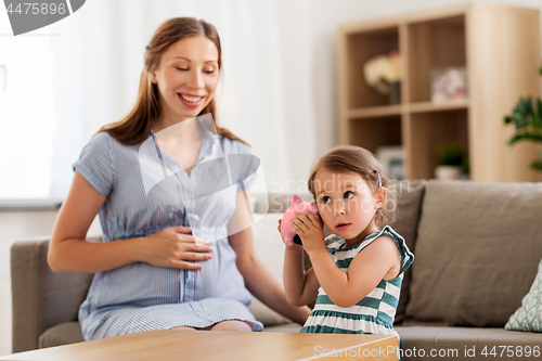 Image of pregnant mother and daughter with piggy bank