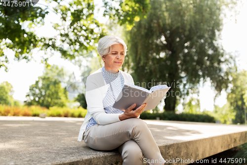 Image of senior woman reading book at summer park