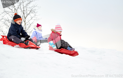 Image of kids sliding on sleds down snow hill in winter