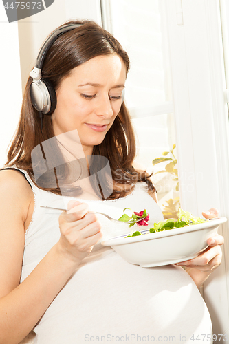 Image of pregnant woman eat salad and listening to music