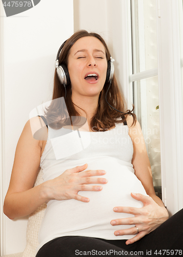 Image of happy pregnant woman singing and listening to music