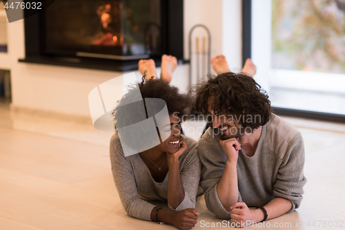 Image of multiethnic couple lying on the floor  in front of fireplace