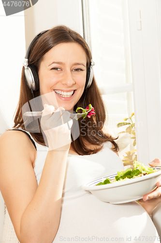 Image of pregnant woman eat salad and listening to music