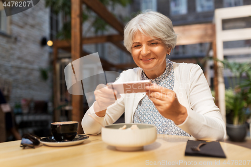 Image of senior woman photographing food at street cafe