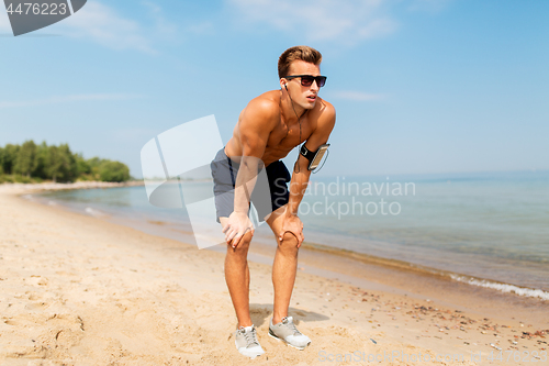 Image of male runner with earphones and arm band on beach