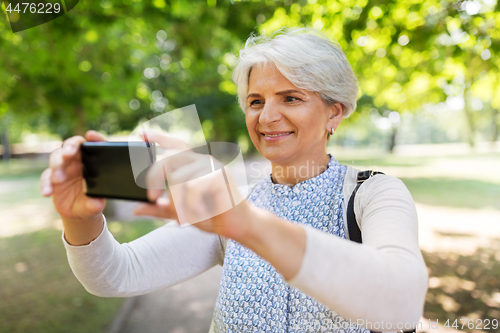 Image of senior woman photographing by cell at summer park