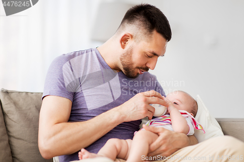 Image of father feeding baby daughter from bottle at home