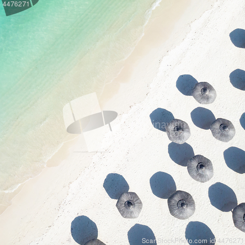 Image of Aerial view of amazing tropical white sandy beach with palm leaves umbrellas and turquoise sea.