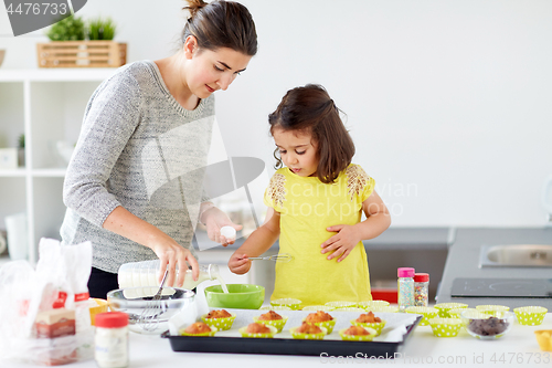 Image of happy mother and daughter baking muffins at home