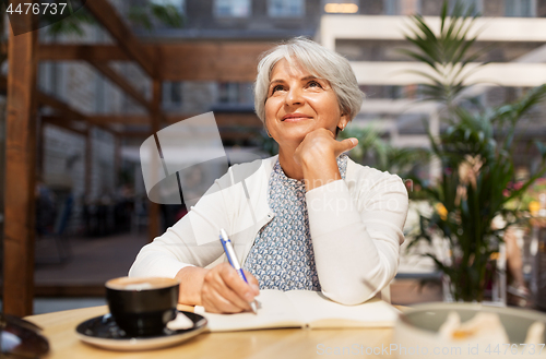 Image of senior woman with notebook dreaming at street cafe