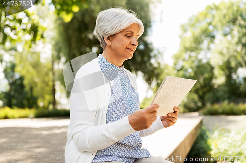 Image of senior woman reading newspaper at summer park