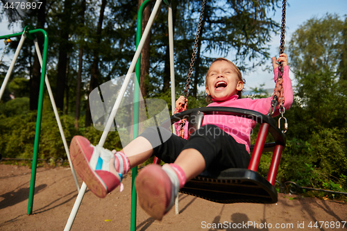 Image of Little girl with funny facial expression swinging on the swings