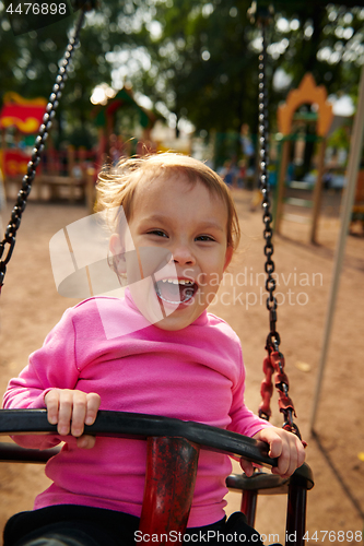 Image of Little girl with funny facial expression swinging on the swings