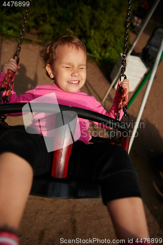 Image of Little girl with funny facial expression swinging on the swings