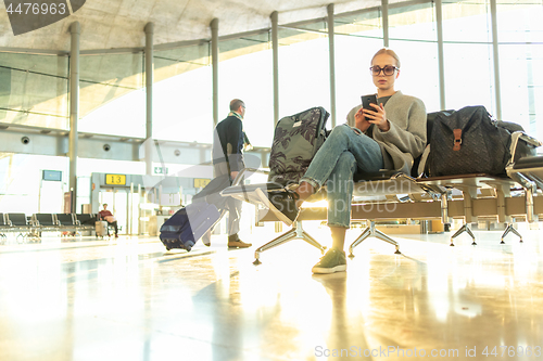 Image of Female traveler using her cell phone while waiting to board a plane at departure gates at airport terminal.