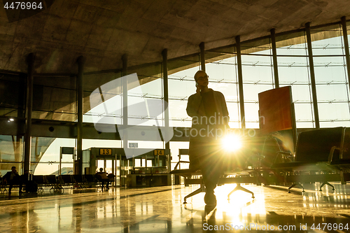 Image of Female traveler talking on her cell phone while waiting to board a plane at departure gates at airport terminal.