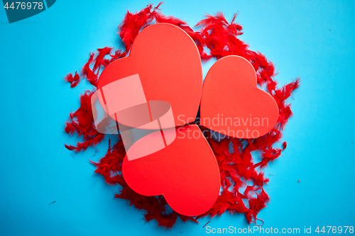 Image of Three red, heart shaped gift boxes placed on blue background among red feathers