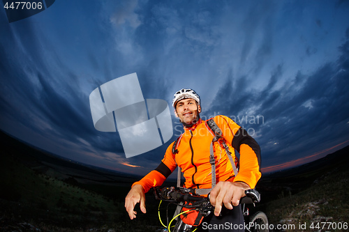 Image of cyclist standing with mountain bike on trail at sunset