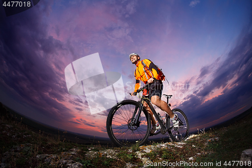 Image of cyclist standing with mountain bike on trail at sunset