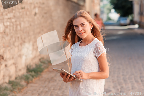 Image of beautiful young woman in white dress using tablet