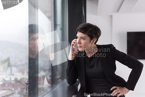 Image of Elegant Woman Using Mobile Phone by window in office building