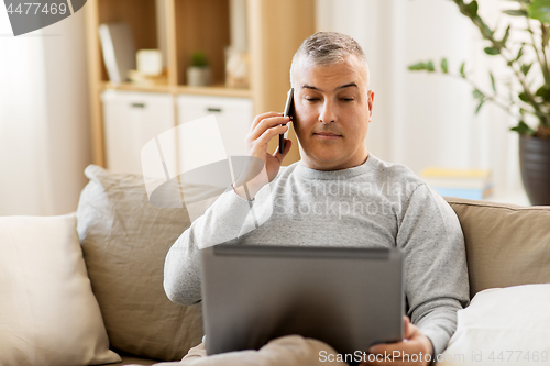 Image of man with laptop calling on smartphone at home