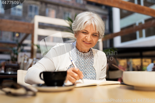 Image of senior woman writing to notebook at street cafe