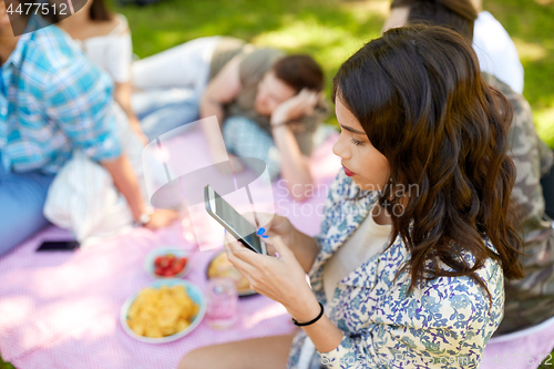 Image of woman using smartphone at picnic with friends