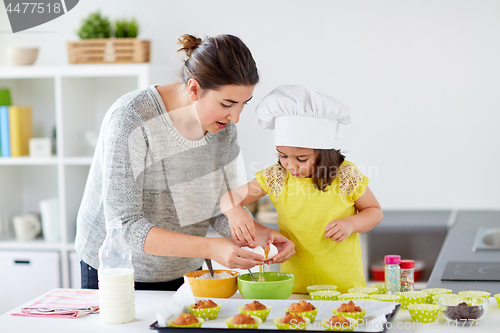 Image of happy mother and daughter baking muffins at home