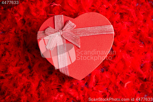 Image of Heart shaped boxed gift, placed on red feathers background