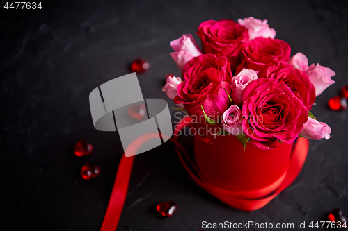 Image of Pink roses bouquet packed in red box and placed on black stone background