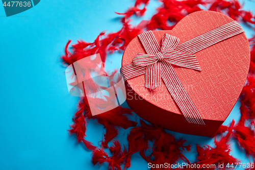 Image of Red, heart shaped gift box placed on blue background among red f