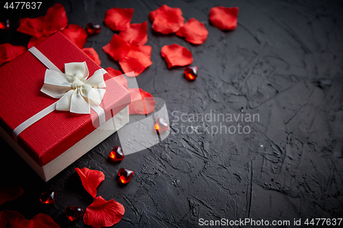 Image of Gift box on black stone table. Romantic holiday background with rose petals