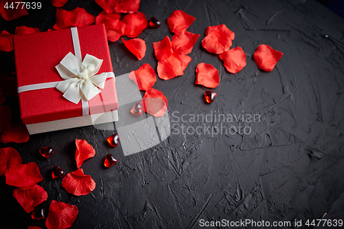 Image of Gift box on black stone table. Romantic holiday background with rose petals