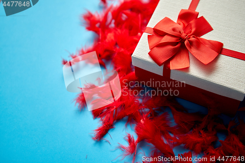 Image of Box with a gift, tied with a ribbon placed on red feathers