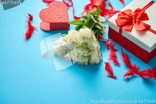 Image of Bouquet of white roses with red bow on blue background. Boxed gift on side