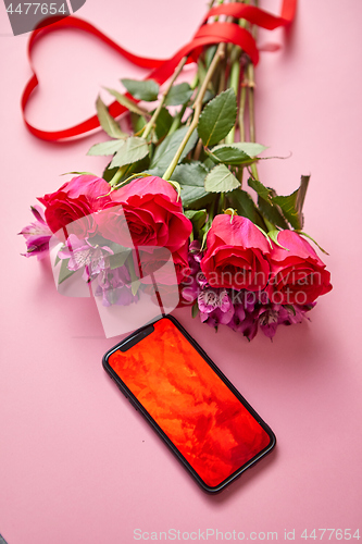 Image of Pink roses bouquet with hart shaped bow and mobile phone with copy space screen